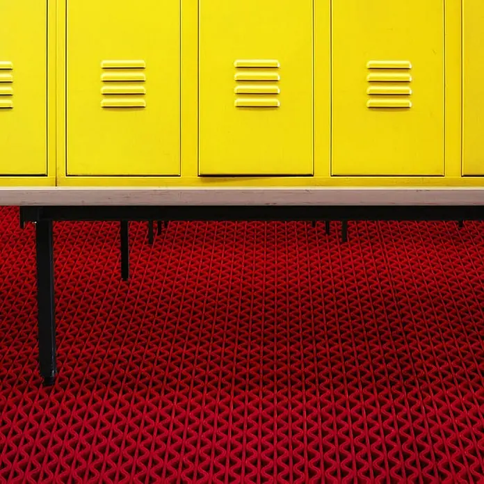 Floordirekt Antirutschmatte Anti-Slip für Barfußzonen - UV-beständig - Rot - 90 x 600 cm - Rot - Helle gelbe Schließfächer über einer Holzbank mit schwarzen Beinen, vor einer leuchtend roten gemusterten Bodenmatte.