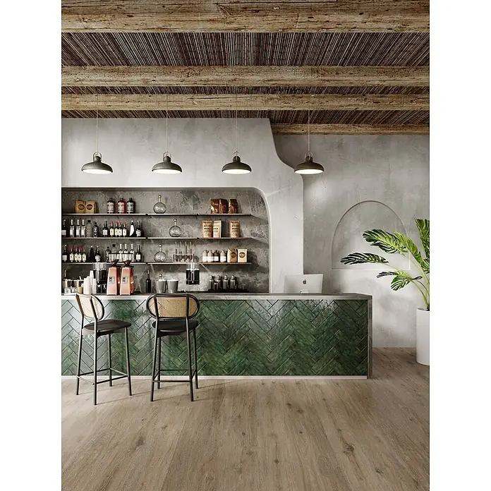 Wandfliese JULIET VERT – 7.5 x 30 cm, Zellige-Optik, Brillant -  - Modernes Café-Interieur mit grünem Fischgrät-Bartresen, strukturierter Holzdecke und glatten Betonwänden.