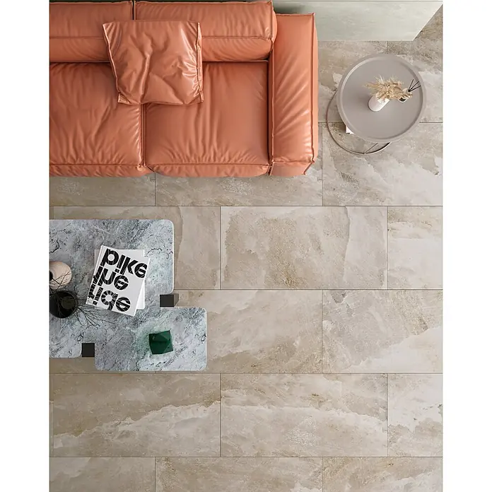 Feinsteinzeugfliese SALT CAVE TAUPE – 60 x 120 cm, Steinoptik, Mat -  - Rechteckige hellbeige Bodenfliesen in Natursteinoptik schaffen einen warmen Wohnzimmerboden unter einem orangefarbenen Sofa und Tischen.