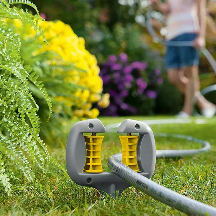 Neptun Schlauch- & Kabelführung - Kunststoff, Erdspieß - Bild eines grauen Rasensprengers mit gelben Rollen, der auf grünem Gras steht und einen Gartenschlauch hält.