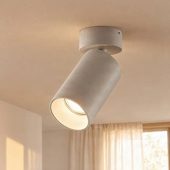 Arcchio Wandstrahler innen, Deckenstrahler 350° drehbar, 90° schwenkbar -  - Grauer Deckenstrahler aus Beton, an einer hellen Decke montiert und schräg ausgerichtet, strahlt warmes Licht aus.