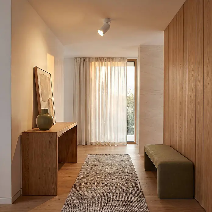 Arcchio Wandstrahler innen, Deckenstrahler 350° drehbar, 90° schwenkbar -  - Heller, moderner Flur mit hellen Holzmöbeln, einem strukturierten Teppich, transparenten Vorhängen und einem weißen Deckenstrahler.
