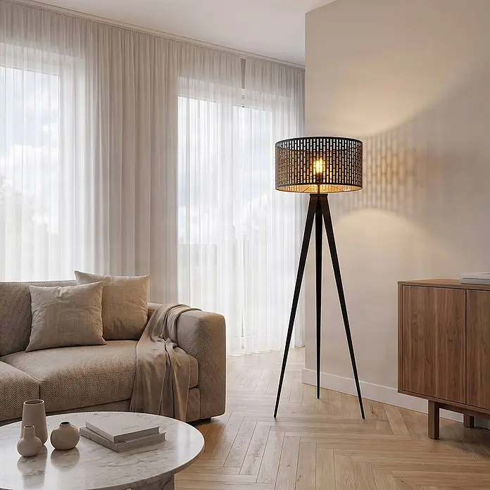 Lindby Stehlampe Dreibein schwarz gold mit Fußschalter, ohne Leuchtmittel -  - Schwarze Dreifuß-Stehleuchte mit zylindrischem, perforiertem Metallschirm, erzeugt geometrische Lichtmuster, in einem modernen Wohnzimmer.