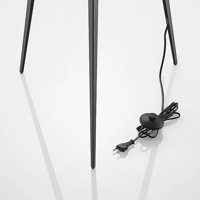 Lindby Stehlampe Dreibein schwarz gold mit Fußschalter, ohne Leuchtmittel -  - Nahaufnahme einer schwarzen Lampenbasis mit schlanken Metallbeinen, Stromkabel, Fußschalter und Stecker.