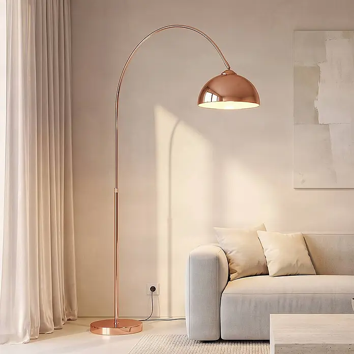 Lindby Stehlampe in kupfer, Bogenlampe Wohnzimmer -  - Roségoldene Bogen-Stehleuchte mit Kuppelschirm, die warmes Licht über einem Sofa in einem modernen Wohnzimmer spendet.
