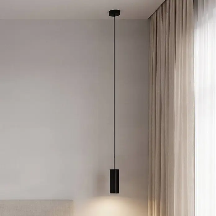 Arcchio Pendelleuchte in schwarz, Hängelampe -  - Minimalistische schwarze zylindrische Pendelleuchte hängt von der Decke und beleuchtet einen Bereich über einem Bettkopfteil neben einem Vorhang.