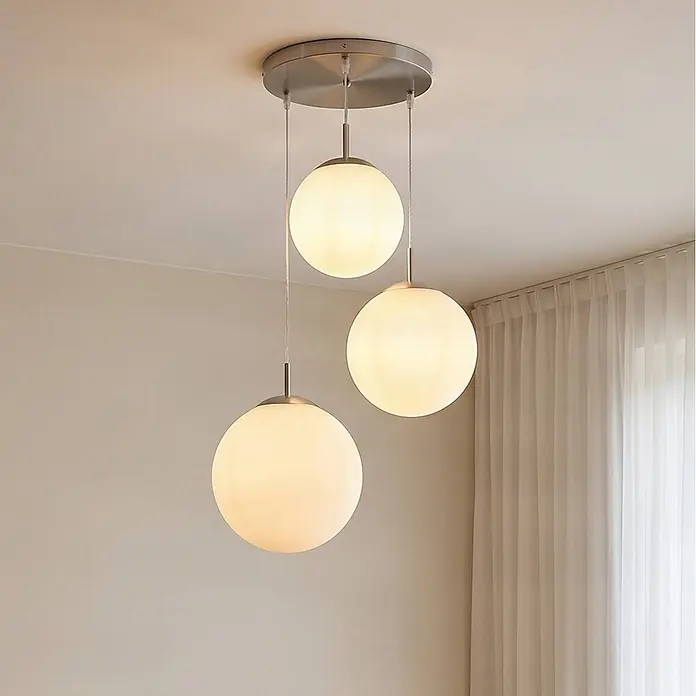 Lindby Pendelleuchte in nickel matt, weiß, Hängelampe -  - Drei moderne Pendelleuchten mit kugelförmigen Opalglasschirmen und gebürsteten Metallbeschlägen hängen von einer Deckenplatte.