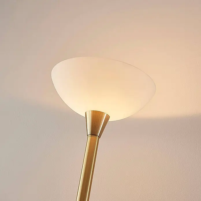 Lindby Stehlampe / Deckenfluter Metall Glas, Standleuchte Messing matt -  - Nahaufnahme einer Stehlampe mit weißem Milchglasschirm und goldenem Metallkörper, die warmes Licht nach oben auf eine Wand wirft.