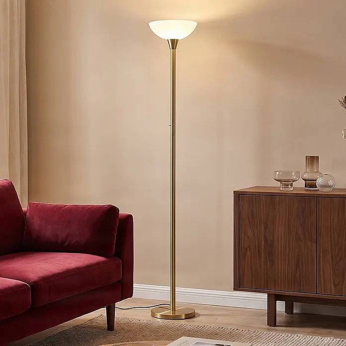 Lindby Stehlampe / Deckenfluter Metall Glas, Standleuchte Messing matt -  - Goldene Stehlampe mit weißem Glasschirm spendet Umgebungslicht in einem modernen Wohnzimmer neben einem roten Sofa.