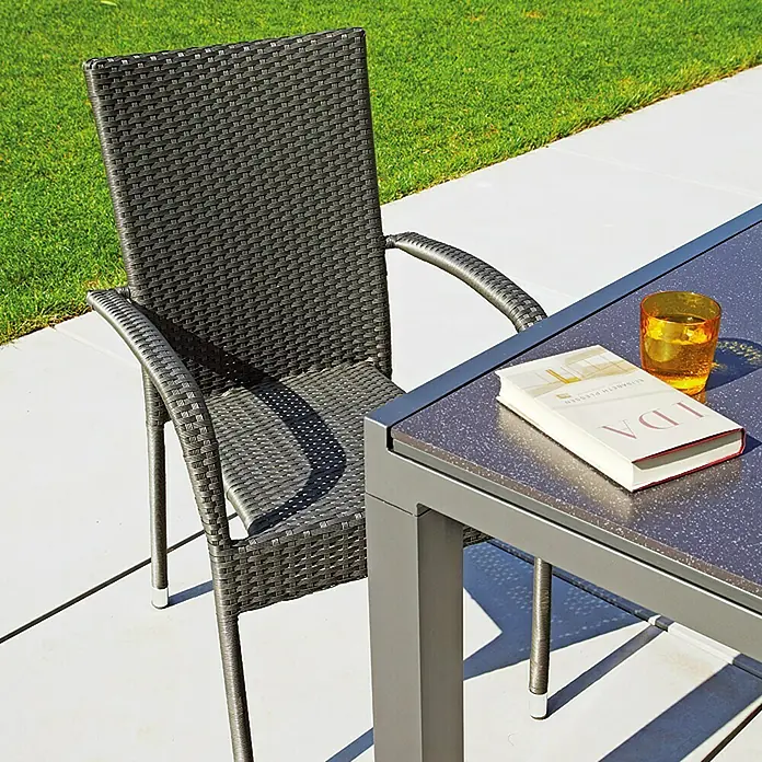 Sunfun Neila Gartensessel - B x T x H: 56 x 63 x 94 cm, Polyrattan, Stapelbar, Silbergrau - Nahaufnahme eines grauen Rattan-Gartenstuhls neben einem Tisch mit einem Buch und einem Glas.