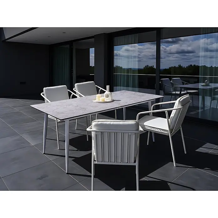Esstisch TOLENTINO in Grau/Weiß - (W) 90 x (H) 75 x - L - Modernes Outdoor-Essset mit hellgrauem Tisch und weißen Stühlen mit Kissen auf dunkler Terrasse, Blick auf Landschaft.