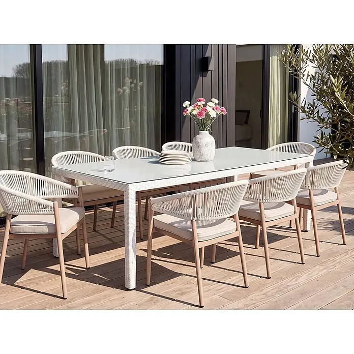 Esstisch ITALY in Weiß - (W) 100 x (H) 74 x - L - Weißer Rattan-Esstisch mit Glasplatte und acht Stühlen mit hellen Holzrahmen, geflochtenen Lehnen und beigen Polstern auf einer Holzterrasse.