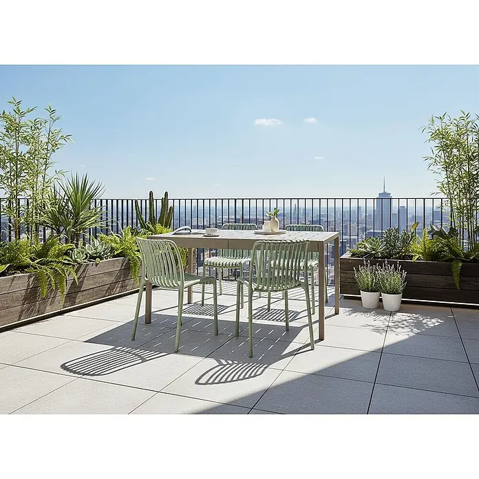 Esstisch BARTICA in Beige - (W) 84 x (H) 76 x - L - Eine Outdoor-Essgruppe auf einer Terrasse mit Stadtblick, bestehend aus einem hellbeigen Tisch und vier hellgrünen Lattenstühlen.
