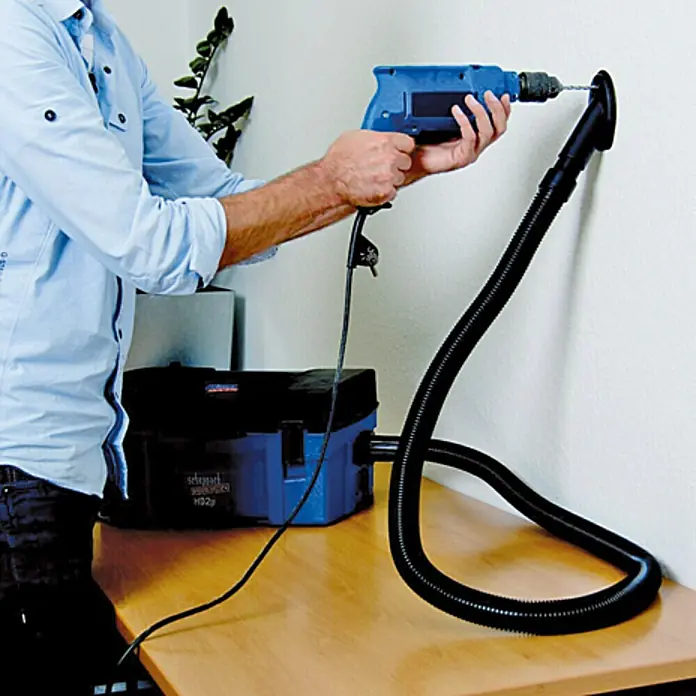 Scheppach Equipo de aspiración HD2P - Potencia de aire máx.: 120 m³/h, Capacidad del depósito: 5 l, 1.250 W - Un hombre perfora una pared con un taladro, mientras una aspiradora aspira el polvo. ¡Práctico para un trabajo limpio!