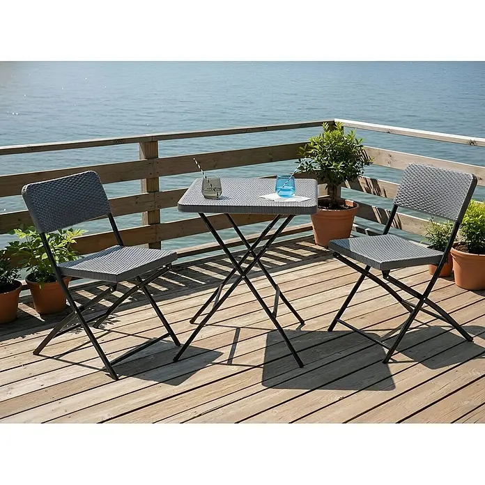 3-tlg Bistro Set TRAPPETO in Grau/Schwarz -  - Ein graues Bistrotisch-Set in Rattanoptik mit Klapptisch und zwei Stühlen, auf einer Holzterrasse am Meer.