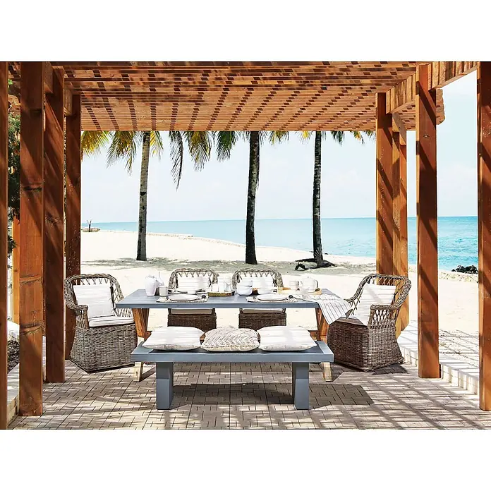 13-tlg Gartentisch Set MAROS/OLBIA in Naturfarben/Grau/Beige -  - Outdoor-Essgruppe unter einer Holzpergola, mit grauem Tisch und Bank, sowie Korbstühlen mit weißen Kissen, am Strand.