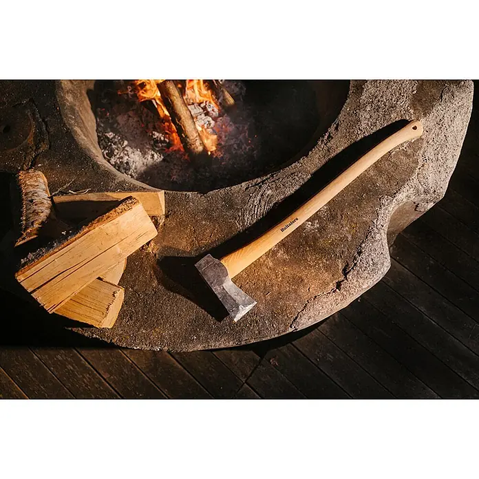Hultafors KVILLINGE Spaltaxt -  - Hultafors Axt mit Holzgriff und Metallkopf, ruhend auf einer steinernen Feuerschale neben Brennholz und einem brennenden Feuer.
