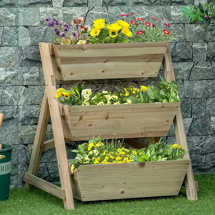 SONNENH Blumentreppe aus Holz mit 3 Ebenen, 71 x 61 x 77 cm -  - Dreistöckiges hellbraunes Holz-Pflanzgefäß mit bunten Blumen und Grünpflanzen, vor einer Steinmauer.