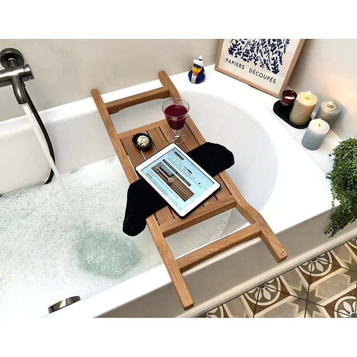 Badewannenablage Holz Cara aus edlem Teak-Kernholz samtweich geschliffen -  - Hölzernes Badewannenbrett mit Tablet, Getränk und Snackschale über einer Badewanne mit fließendem Wasser.