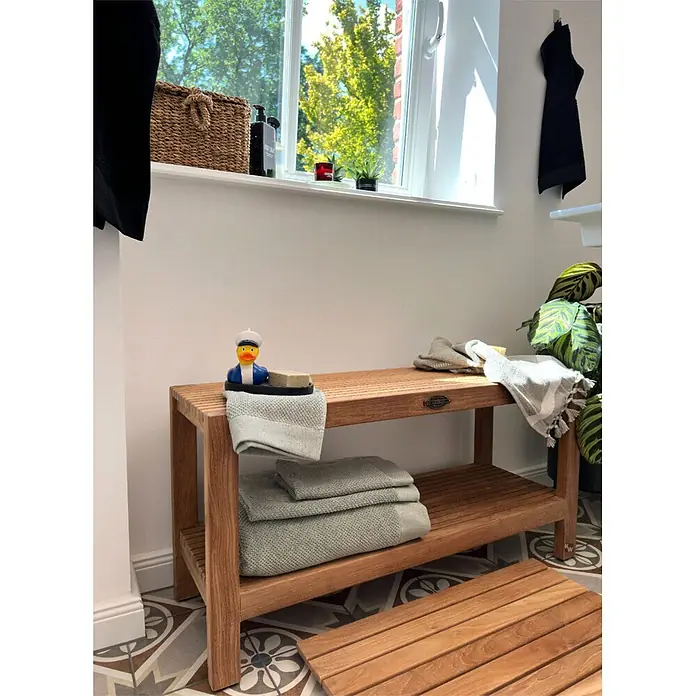 Badregal Holz Bella Teak massiv mit Gummifüßen montiert geliefert -  - Holzlamellenbank mit zwei Ablagen und passender Lattenrost-Badematte auf gemustertem Boden.
