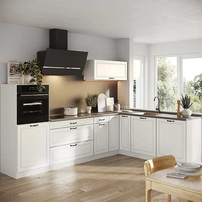Eckküche R-Line 287 cm Weiß Landhaus Art.-Nr. 68215 -  - Eine weiße Küche mit klassischen Paneelschränken, schwarzem integrierten Ofen, Dunstabzugshaube und Spüle, vor warmem Spritzschutz und natürlichem Licht.