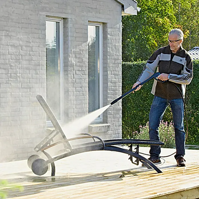 Nilfisk Hidrolimpiadora de alta presión E 145.4-9 Power X-Tra - 145 bar, 2.100 W, Capacidad de bombeo: 500 l/h - Un hombre usa una hidrolavadora para limpiar una tumbona en un patio de madera.