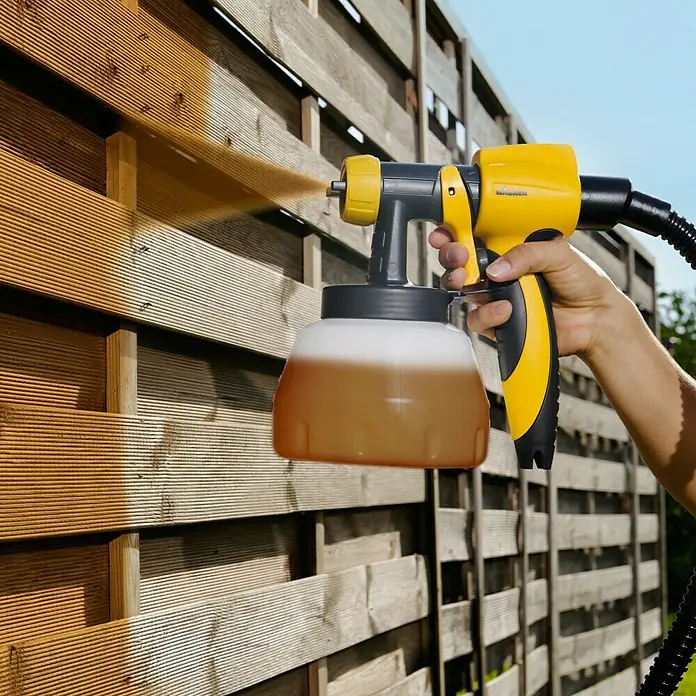 Wagner Sprühaufsatz Wood & Metal EXTRA Large - Geeignet für: Dünnflüssige lösemittel- & wasserbasierte Materialien - Holzzaun wird mit einer gelben Farbspritzpistole besprüht, die eine gleichmäßige Schicht auf das Holz aufträgt.