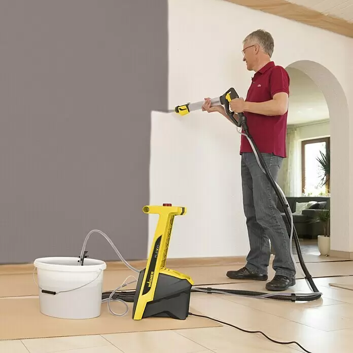 Wagner Farbsprühsystem W 950 Flexio - 630 W, Förderleistung: 0,525 l/min - Mann streicht Wand grau mit gelb-schwarzem WAGNER FLEXIO Farbsprühsystem, Farbe aus weißem Eimer ziehend.