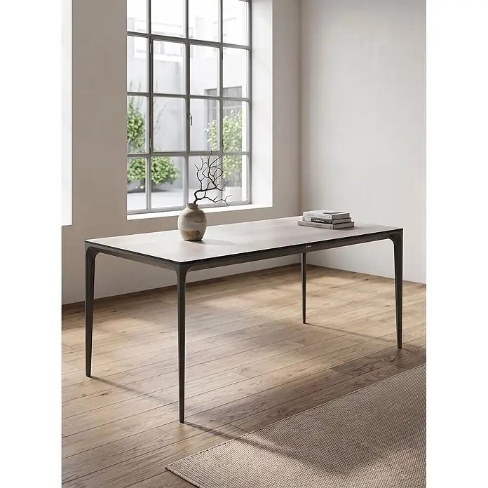 Esstisch SOVARETO in Grau - (W) 90 x (H) 75 x - L - Eleganter Esstisch mit hellgrauer Platte und dunklen, schlanken Beinen, in einem hellen Raum mit großen Fenstern.