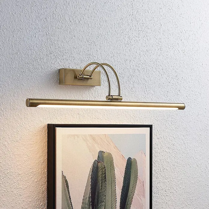 Lucande LED Wandlampe Bilderleuchte altmessing, warmweiß 3.000K -  - Messingfarbene LED-Bilderleuchte an einer Wand, die ein gerahmtes Kunstwerk mit Kaktusmotiv beleuchtet.