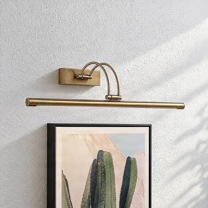 Lucande LED Wandlampe Bilderleuchte altmessing, warmweiß 3.000K -  - Gebürstete Messing-Bilderleuchte an einer strukturierten Wand, die ein gerahmtes Kunstwerk beleuchtet.