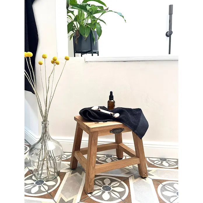 Bad Beistelltisch Holz Loretta Massivholz Hocker ohne sichtbare Schrauben -  - Kleiner Holzschemel mit schwarzem Handtuch und Pflegeprodukten in einem Badezimmer.