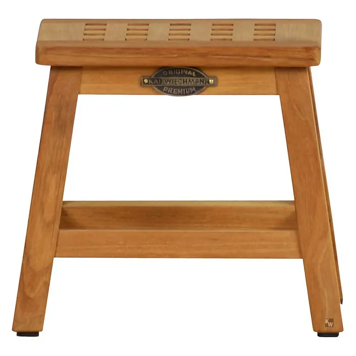 Bad Beistelltisch Holz Loretta Massivholz Hocker ohne sichtbare Schrauben -  - Hellbrauner Holzschemel mit Lattenrostsitzfläche, stabilen Beinen, einer Metallplakette mit „ORIGINAL KAI WIECHMANN PREMIUM“ und einem „KW“-Logo.