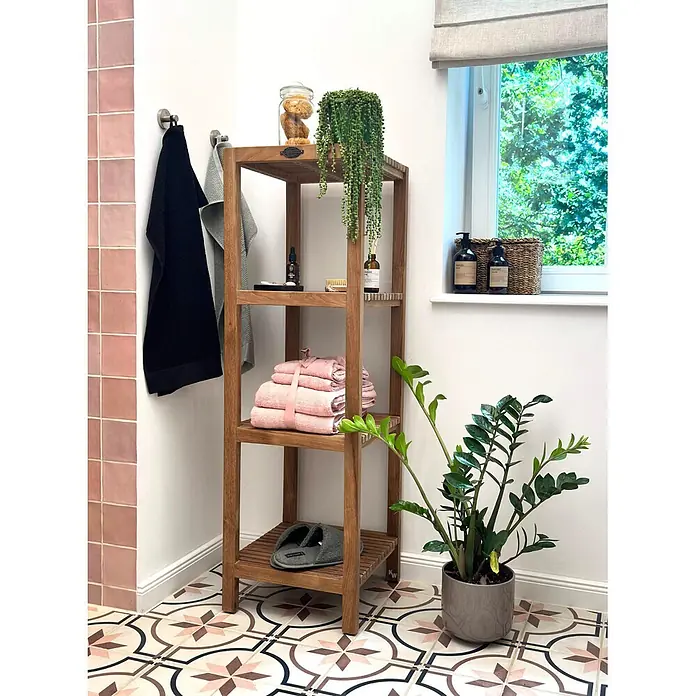 Badregal Holz Mariella Teak Massivholz ideal für Feuchträume 128 cm hoch -  - Hohes Holzregal für das Badezimmer, gefüllt mit rosa Handtüchern, einer Pflanze und Toilettenartikeln, auf gemusterten Bodenfliesen.
