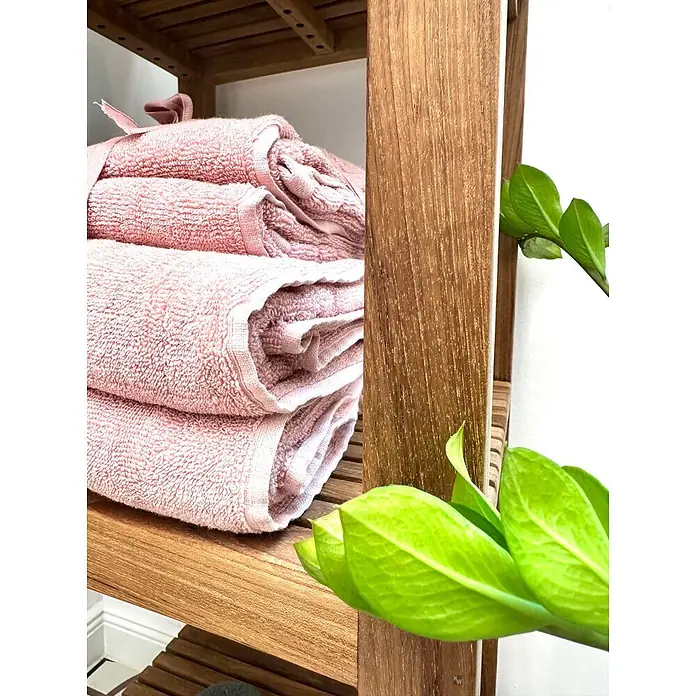 Badregal Holz Mariella Teak Massivholz ideal für Feuchträume 128 cm hoch -  - Gestapelte rosa Handtücher auf einem hellen Holzregal, mit grünen Pflanzenblättern im Vordergrund.
