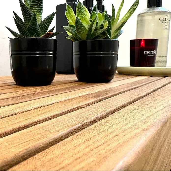 Badregal Holz Tito auch als Bad Sitzbank dank Massivholz-Konstruktion -  - Zwei Topf-Sukkulenten, schwarze Flaschen, eine Kerze und eine 'The Ocean'-Flasche auf einer Holzlamellenfläche.