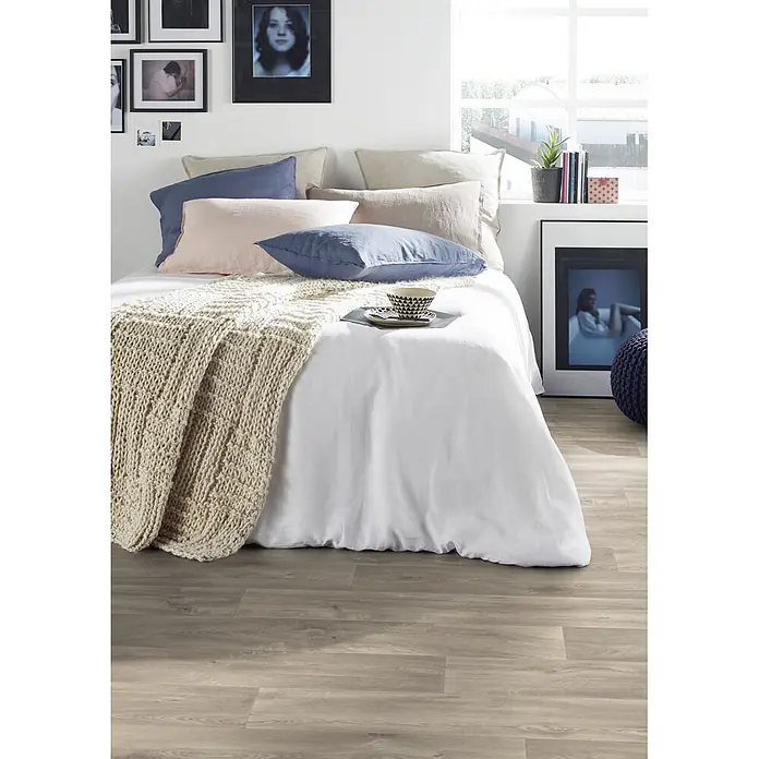 PVC-Boden Meterware Vinylboden 2m Diele Eiche grau antik -  - Ein Bett mit weißer Bettwäsche, verschiedenen Kissen und einer beigen Strickdecke in einem hellen Schlafzimmer.