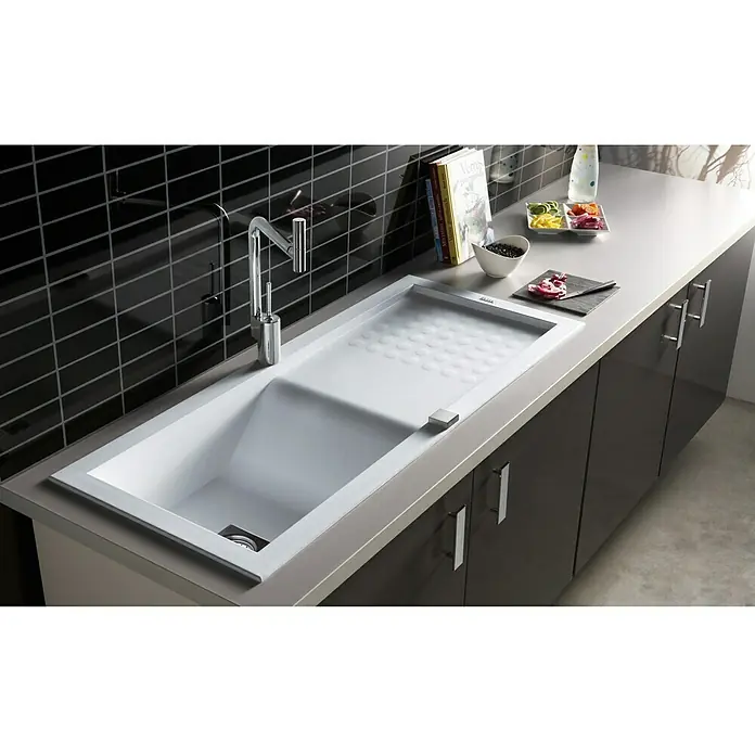 Carea Einbauspüle Vague - 118 x 50 cm, Weiß, Material Spüle: CAREAgranit® - Eine moderne Küchenspüle mit Abtropffläche und Armatur, eingebettet in eine Arbeitsplatte mit dunklen Schränken und stilvollen Accessoires.