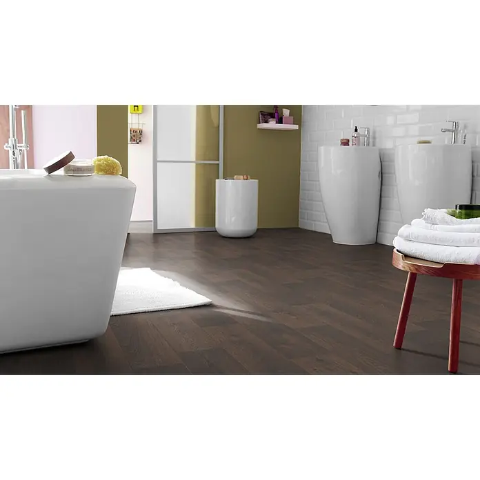 PVC-Boden Meterware Vinylboden 4m Diele Eiche dunkel -  - Dunkler Laminatboden in Holzoptik, verlegt in einem modernen Badezimmer, sichtbar unter einer Badewanne, zwei Waschbecken und einem kleinen Tisch.