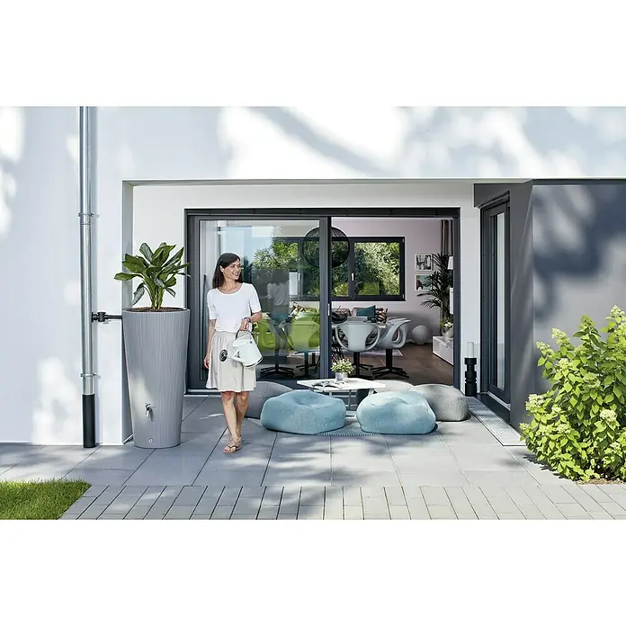 Garantia Classic Line Regenspeicher - 220 l, Zinkgrau - Eine Frau gießt Pflanzen neben einer grauen Regentonnen-Pflanzgefäß-Kombination, die auf einer Terrasse steht.