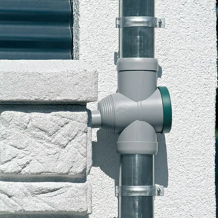 Arves Regenspeicher Maurano - 300 l, Granitfarben, 1 Stk. - Nahaufnahme eines grauen Regenwasserfilters an einer Hauswand mit grauem Rohr und Metallklammern.