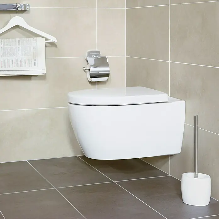 Venus Flakoni WC-Bürstengarnitur - Weiß, Polyresin - Das Bild zeigt eine moderne, wandhängende Toilette in einem Badezimmer mit beigen Fliesen und einem grauen Fliesenboden.