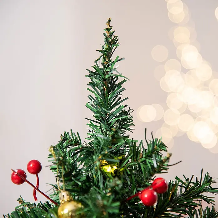 HOMCOM-Weihnachtsbaum-∅40 x H60 cm-Grün -  - Nahaufnahme eines grünen künstlichen Weihnachtsbaums, verziert mit roten Beeren und einer goldenen Kugel, mit verschwommenen Festlichter im Hintergrund.