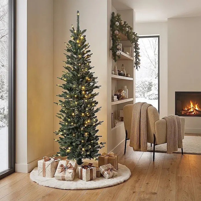ECD Germany Künstlicher Weihnachtsbaum 150 cm mit Beleuchtung, Naturgetreu -  - Ein beleuchteter schlanker künstlicher Weihnachtsbaum mit warmweißen Lichtern und Geschenken an der Basis in einem gemütlichen Wohnzimmer.