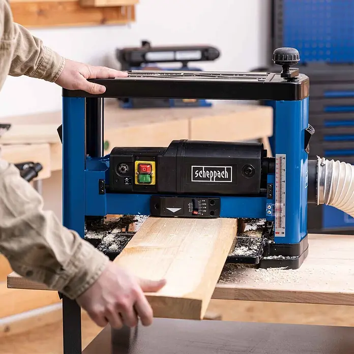 Scheppach Dickenhobelmaschine PLM1800 - 1.500 W, 8.500 U/min, Max. Spanabnahme Dickenhobel: 2,8 mm - Blauer und schwarzer Scheppach Dickenhobel im Einsatz, ein Holzbrett wird von Händen zugeführt.