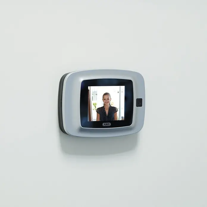 Abus Digitaler Türspion DTS2814 - Stärke Tür: 38 mm - 100 mm, 2,8 ", TFT-Bildschirm, Einbaudurchmesser: 14 mm, Silber/ Schwarz - Silbergrauer digitaler Türspion an der Wand, zeigt eine Frau auf dem Bildschirm. Ein ABUS-Logo ist darunter sichtbar.