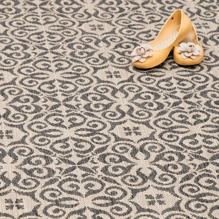 Dekoria Teppich Modern Ethno sand/ anthracite 200x290cm -  - Ein hellbeiger Outdoor-Teppich mit dunkelgrauem Blumen- und Schnörkelmuster, auf dem gelbe Schuhe stehen.