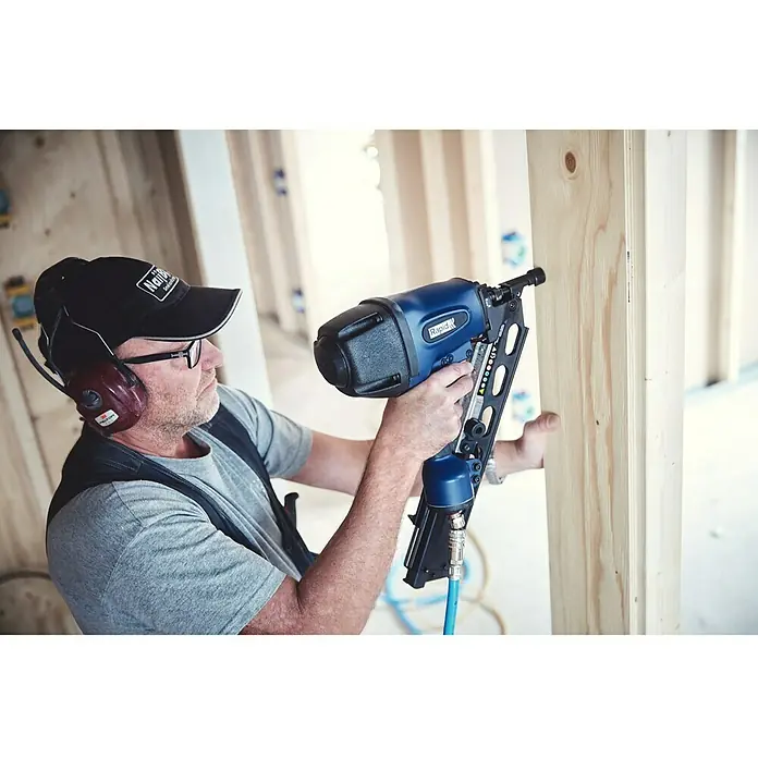 Rapid Druckluft-Streifennagler Rapid PRO PFN3490 - Betriebsdruck: 5 bar - 8 bar, Geeignet für: Streifennägel 50 - 90 mm - Mann benutzt einen Rapid-Druckluftnagler, um Holz zu befestigen. Das Gerät ist blau und schwarz mit einem Magazin für Nägel.