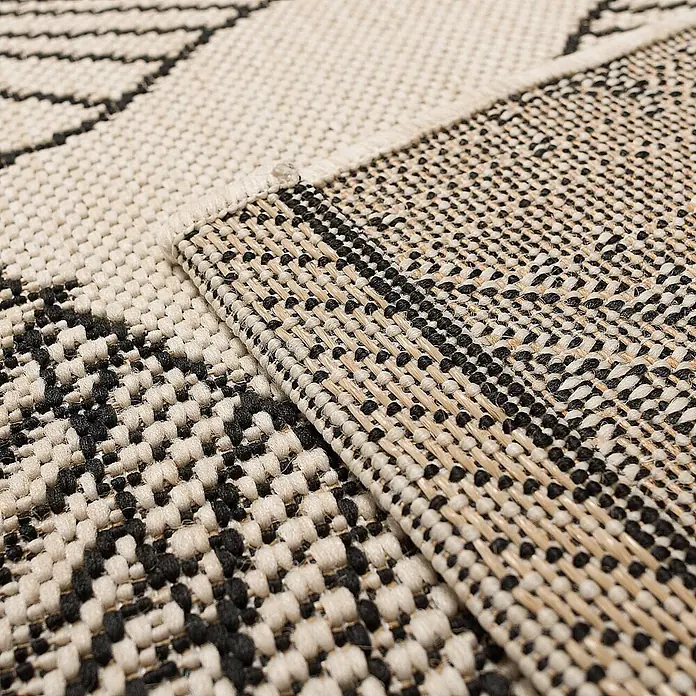 Dekoria Teppich Cottage beige/black 120x170cm -  - Nahaufnahme eines gefalteten schwarz-beigen Webteppichs mit gemusterter Oberseite und texturierter Unterseite.