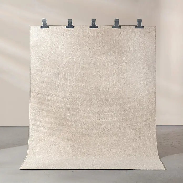 Dekoria Teppich Tivora oatmeal 160x230 cm -  - Hellbeiger Teppich mit dezentem Blattmuster, vertikal an einer Wand hängend und auf einem Betonboden auslaufend.